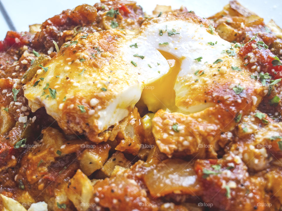 Closeup of poached egg on fried potatoes with tomato sauce