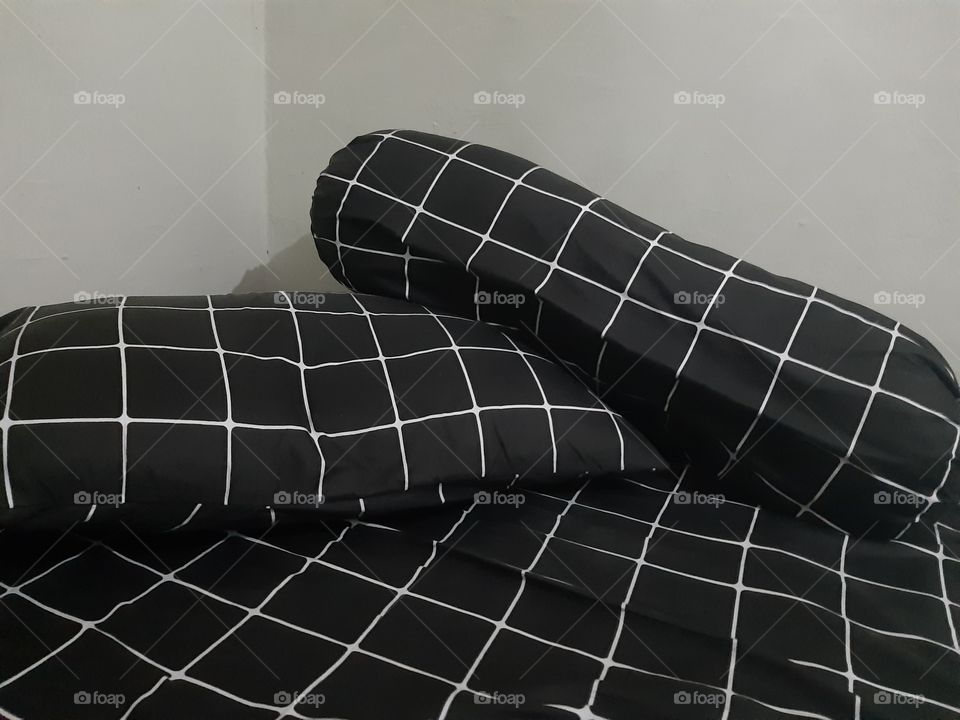 Pillows on the bed covered with balck clothes with rectangular white pattern
