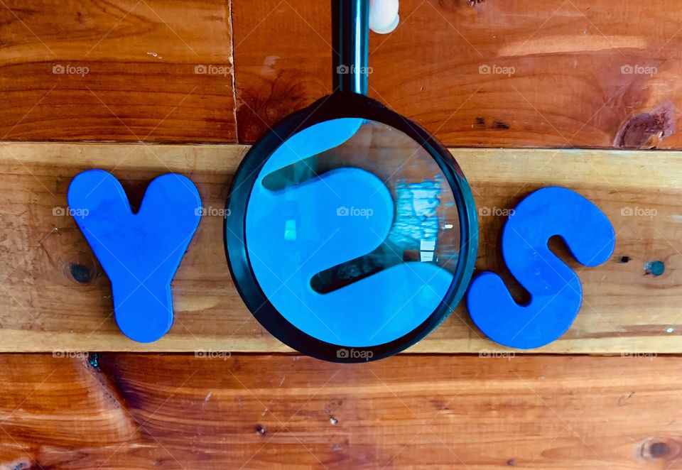 Blue YES Word Written On A Wooden Wall With Enlarged Kids Foam Letter E With Magnifier