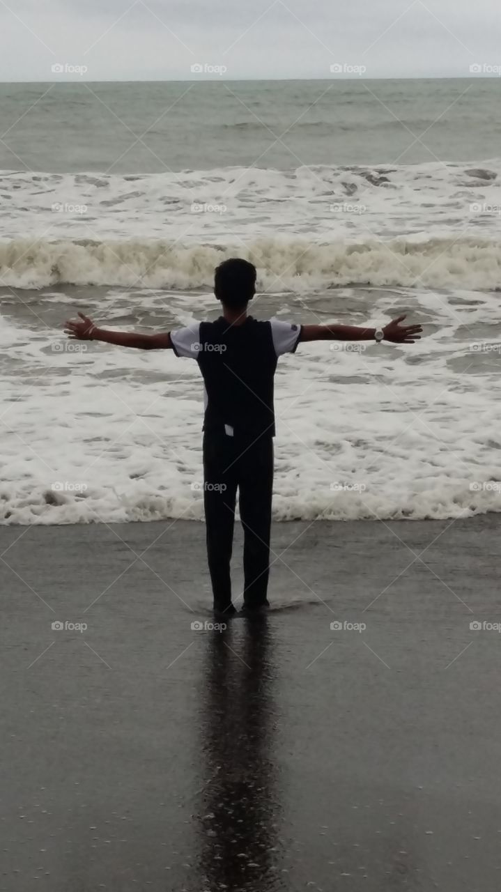 young boy playing by the ocean shoreline in front of a stormy wave