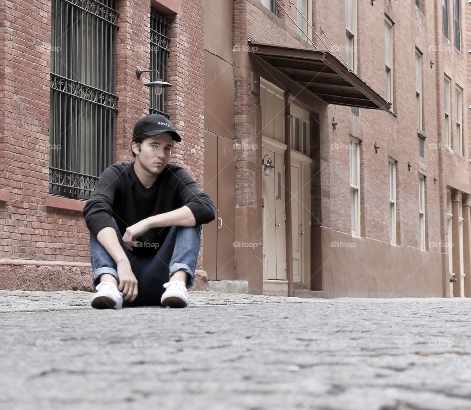 Young man sitting on street near building