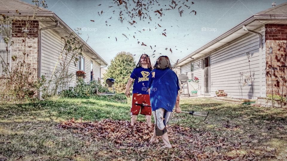 Two girls raking up autumn leaves near house