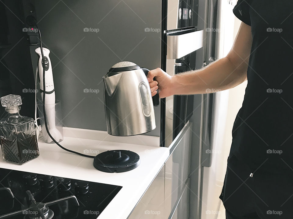 Young man holding metal electric teapot in the kitchen 