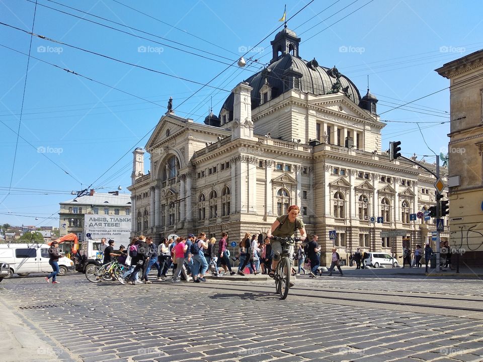 Lviv, Ukraine - April 21, 2018: People cross the road, the woman rides on bicycle, Lviv Theatre of Opera and Ballet on background