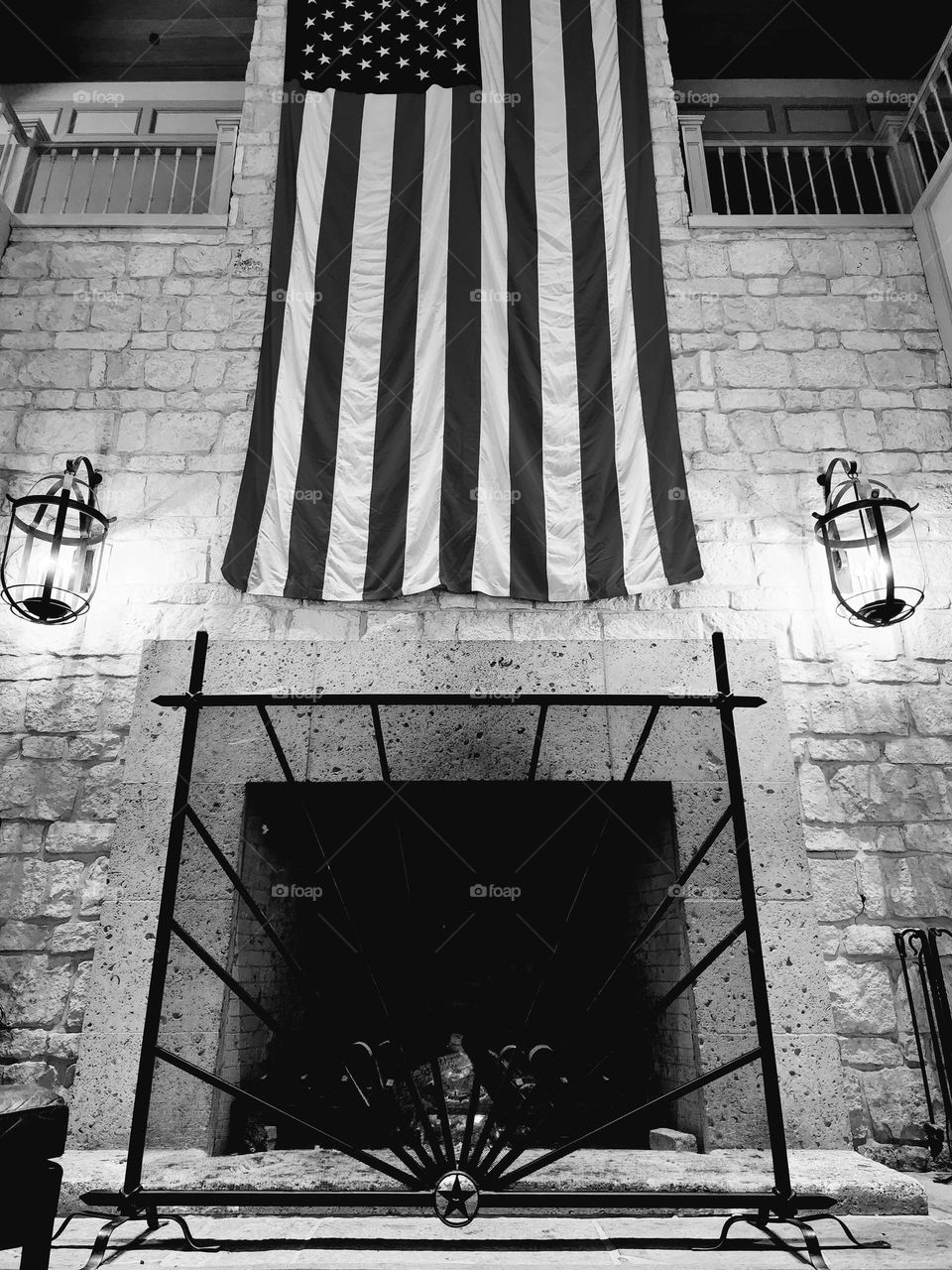 Black and white composition of a dwindling fire in a fireplace and a large American flag draped on the wall