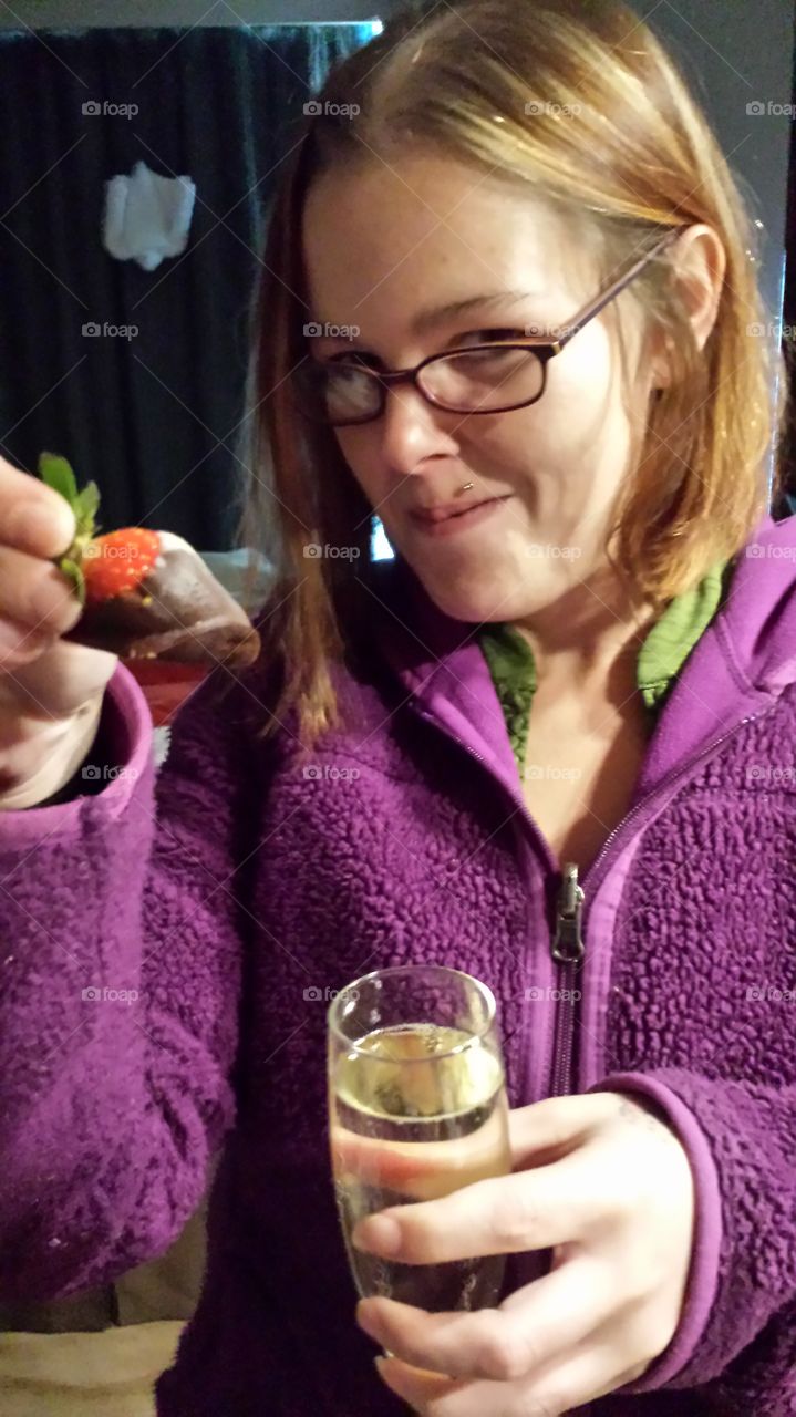 Woman holding chocolate strawberry and glass of drink in hand