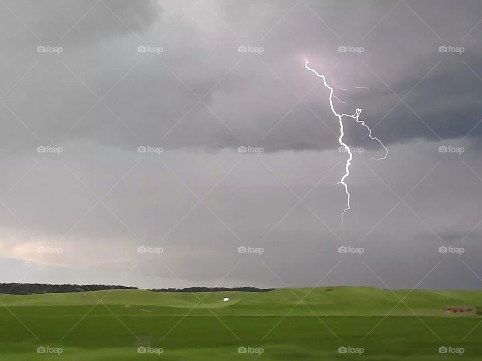 A lightning bolt strikes down from a severe thunderstorm over the plains of eastern Montana, USA.