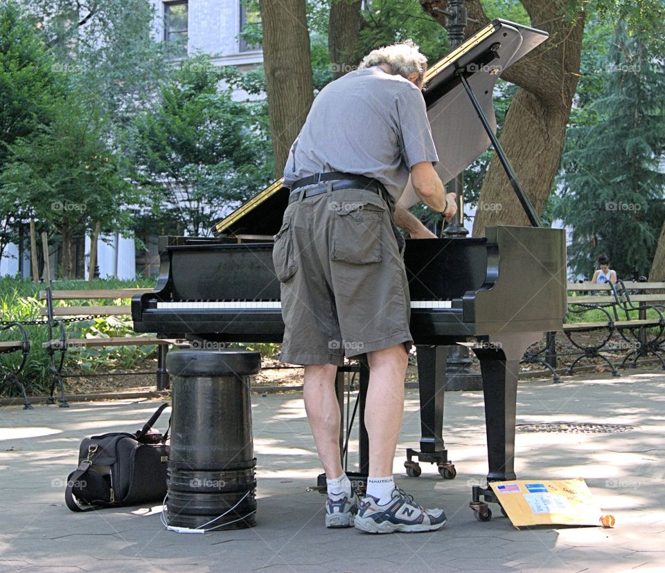 A piano tuner in Washington Square Park, New City tunes
 a piano in sneakers and short pants.