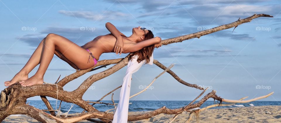 Woman in bikini lying on driftwood at beach