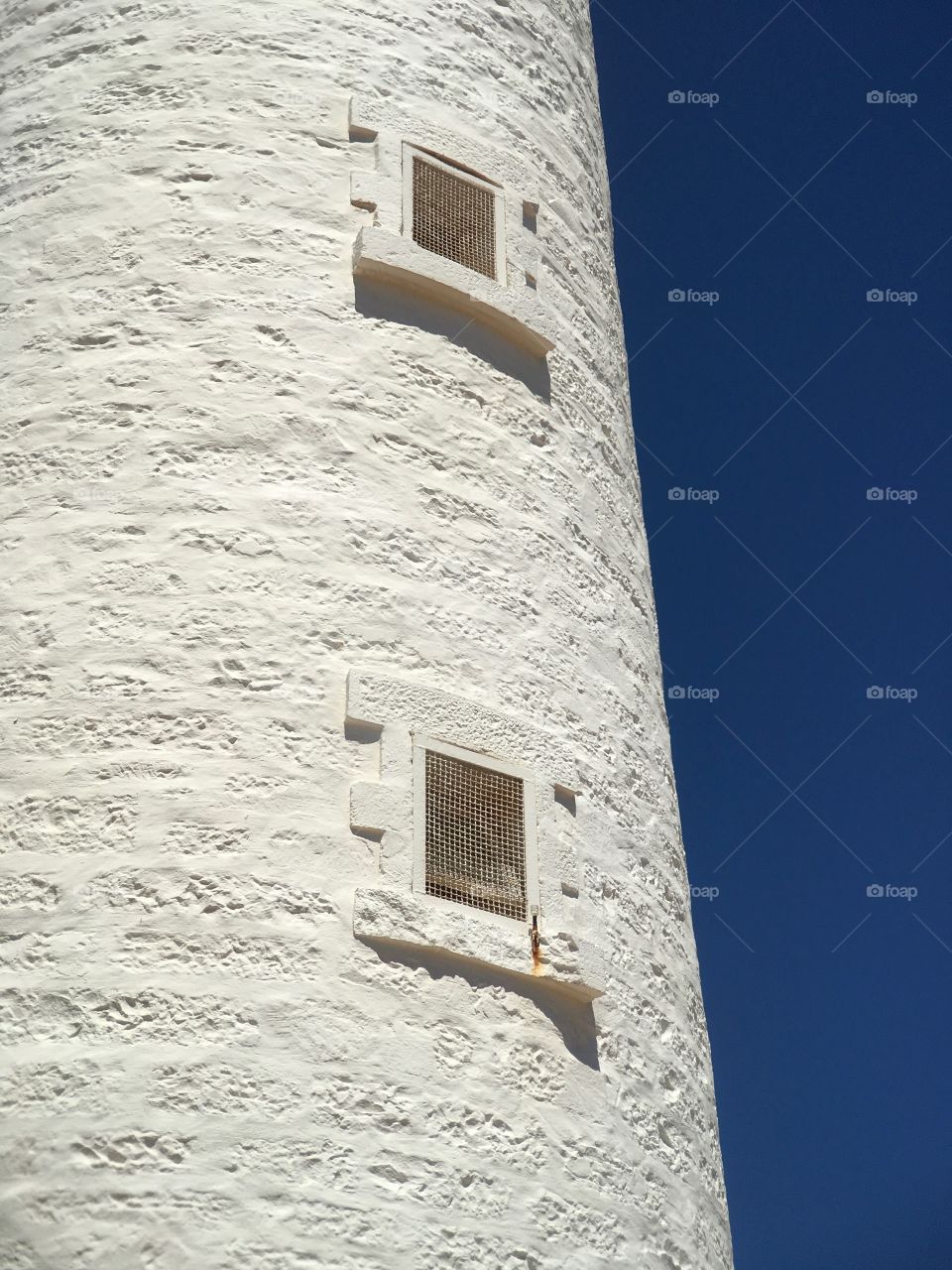 White stone lighthouse against a vivid indigo blue sky minimalistic conceptual with space for text copy
