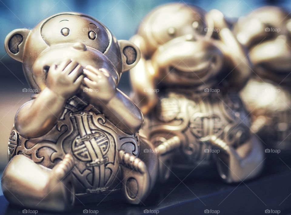Focus on the image is on one of the three wise monkeys - the one who speaks no evil. These figurines are adorned with oriental style attire.