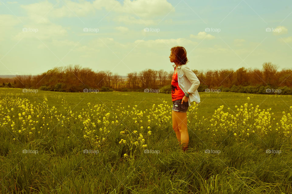 Woman standing in a field of flowers and looking off in the distance