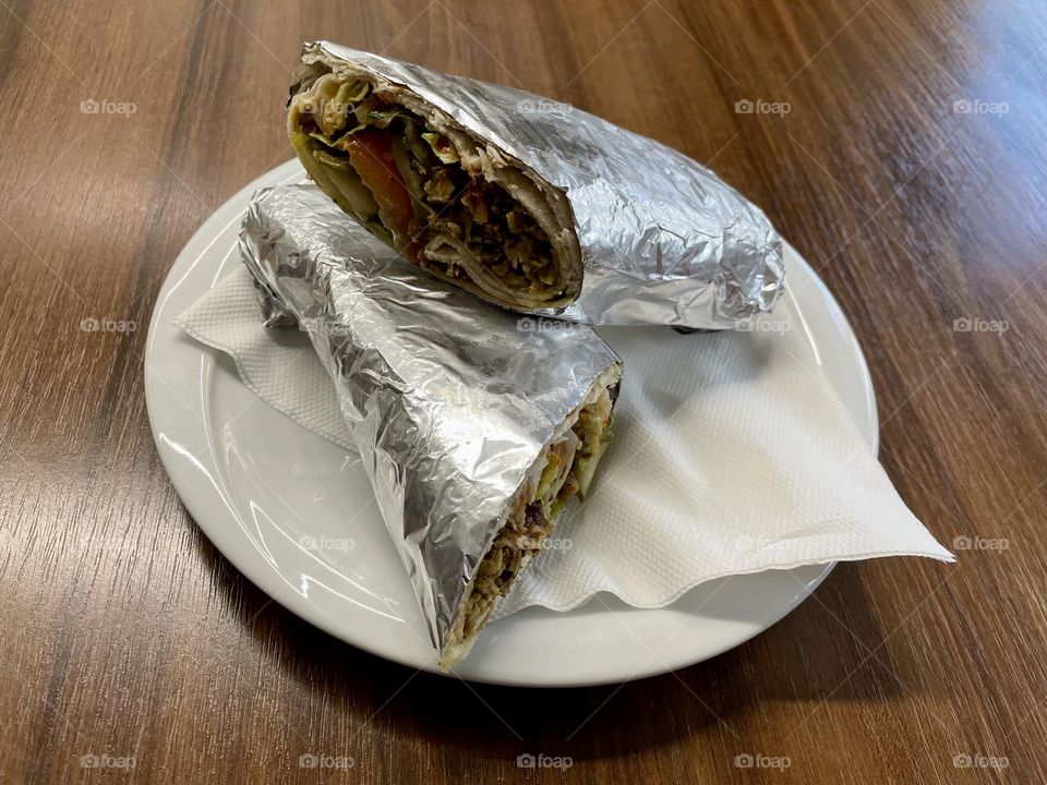 White plate with delicious shawarma wrapped in foil on a wooden table. Delicious Middle Eastern food. Authentic street food.