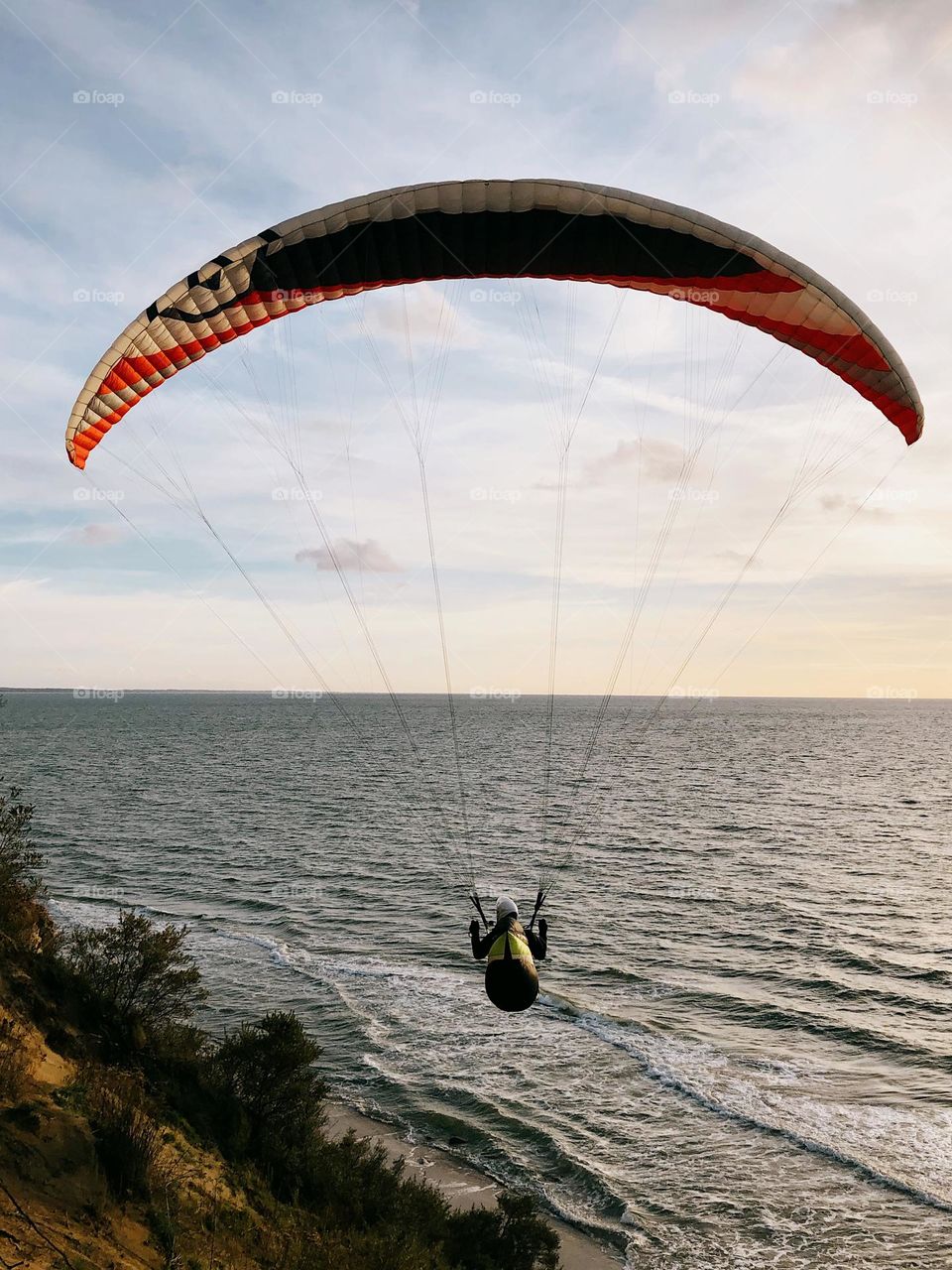 Unrecognisable man flying in a paraglider over the sea, glimmers 