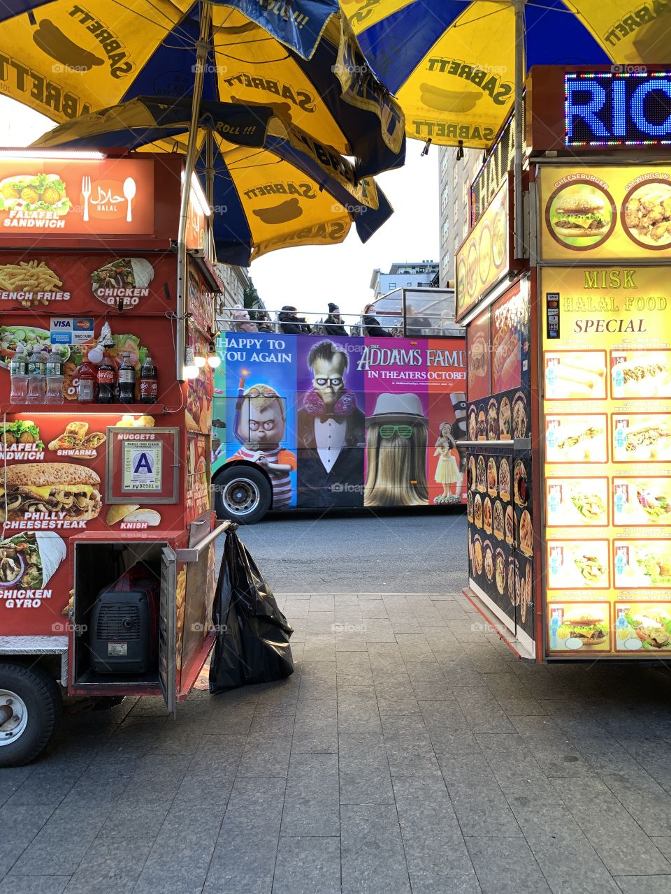 Two half street foods with yellow and blue umbrellas. And at the center a bus with Adams family animated movie. Halal foods.