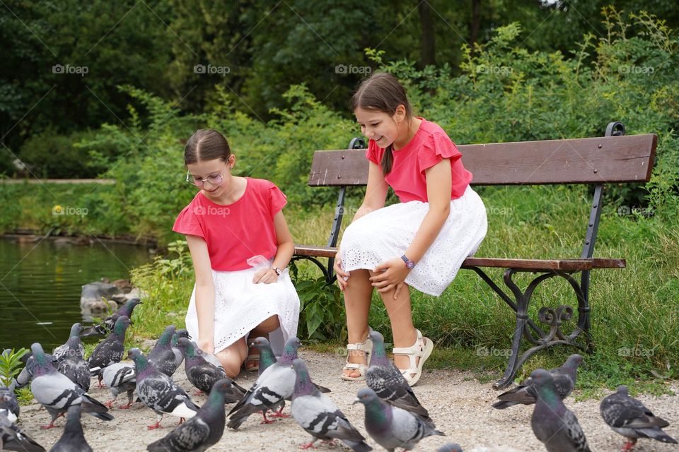 Two girls feeding pigeons in the city park