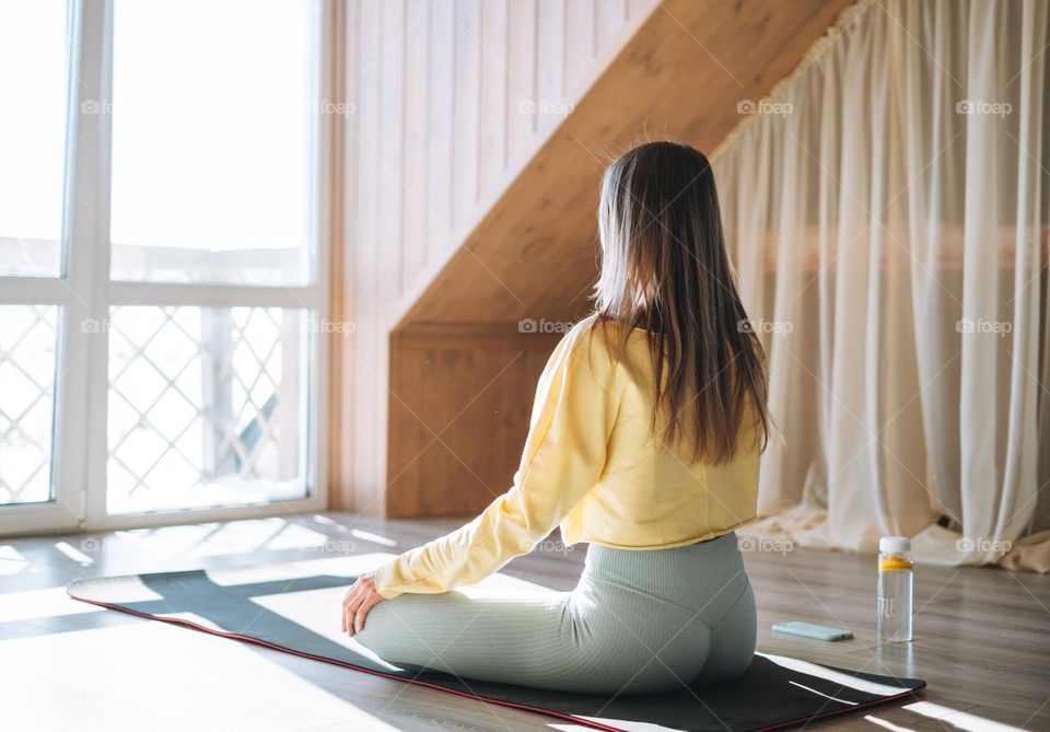 Young slender fitness blonde woman practice morning yoga near the window of home