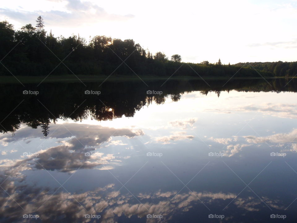 Natural Mirror. Gorgeous mirror smooth lake reflecting sparkling setting sun and clouds