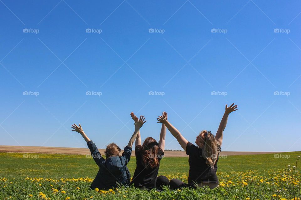 Three girls are sitting on the field with raised hands.