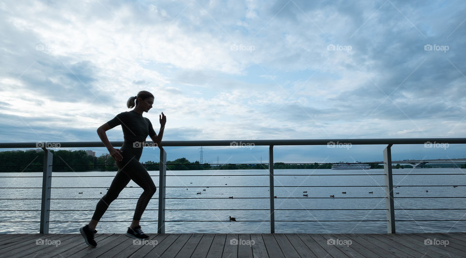 Young woman making workout near water silhouette 