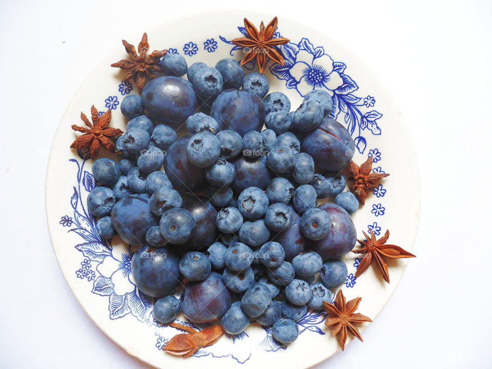 Berries of blueberries and plums on a white plate