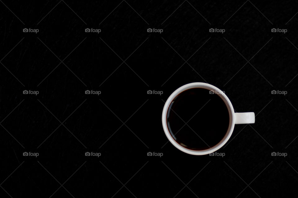 Top view to cup with black coffee on dark background with copy paste.