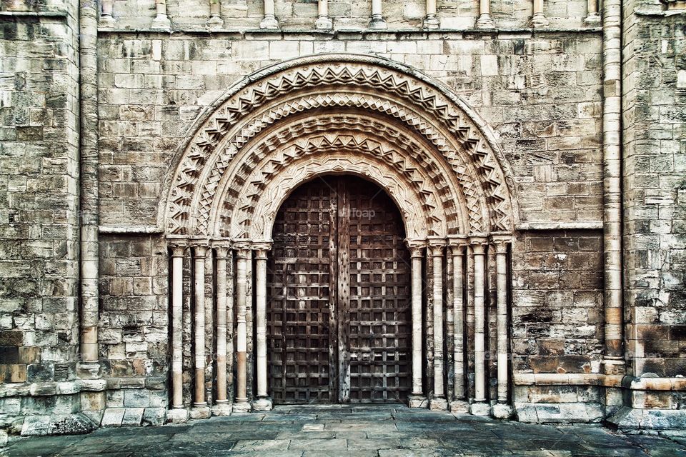 A heavy wooden door into a church surrounded by ornate stone carvings.