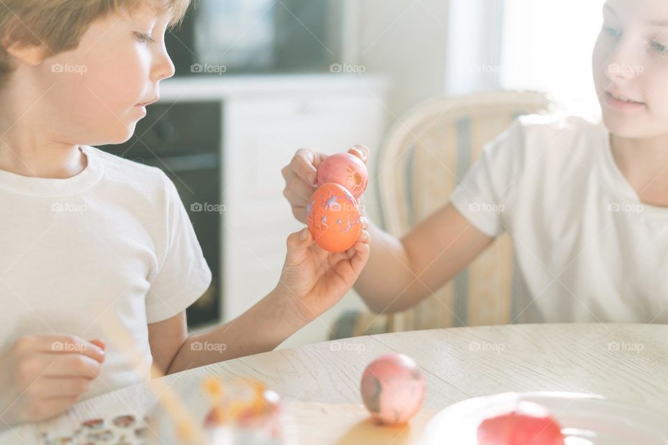 Two siblings brother and sister toddler boy tween girl painting easter eggs on kitchen at home on the spring sunny day