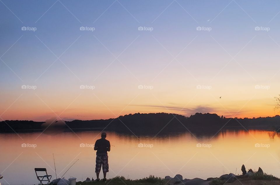 Fisherman on the bank of river, fishing as sunset