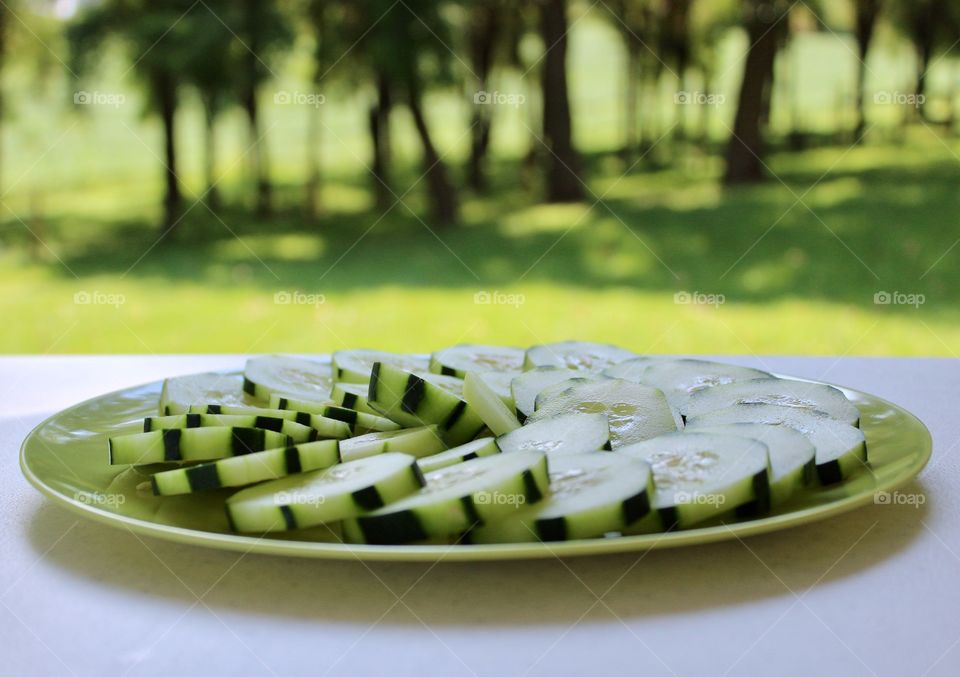 Fruits! - Cucumbers in a spiral pattern on a green plate on a white table against a blurred background of trees