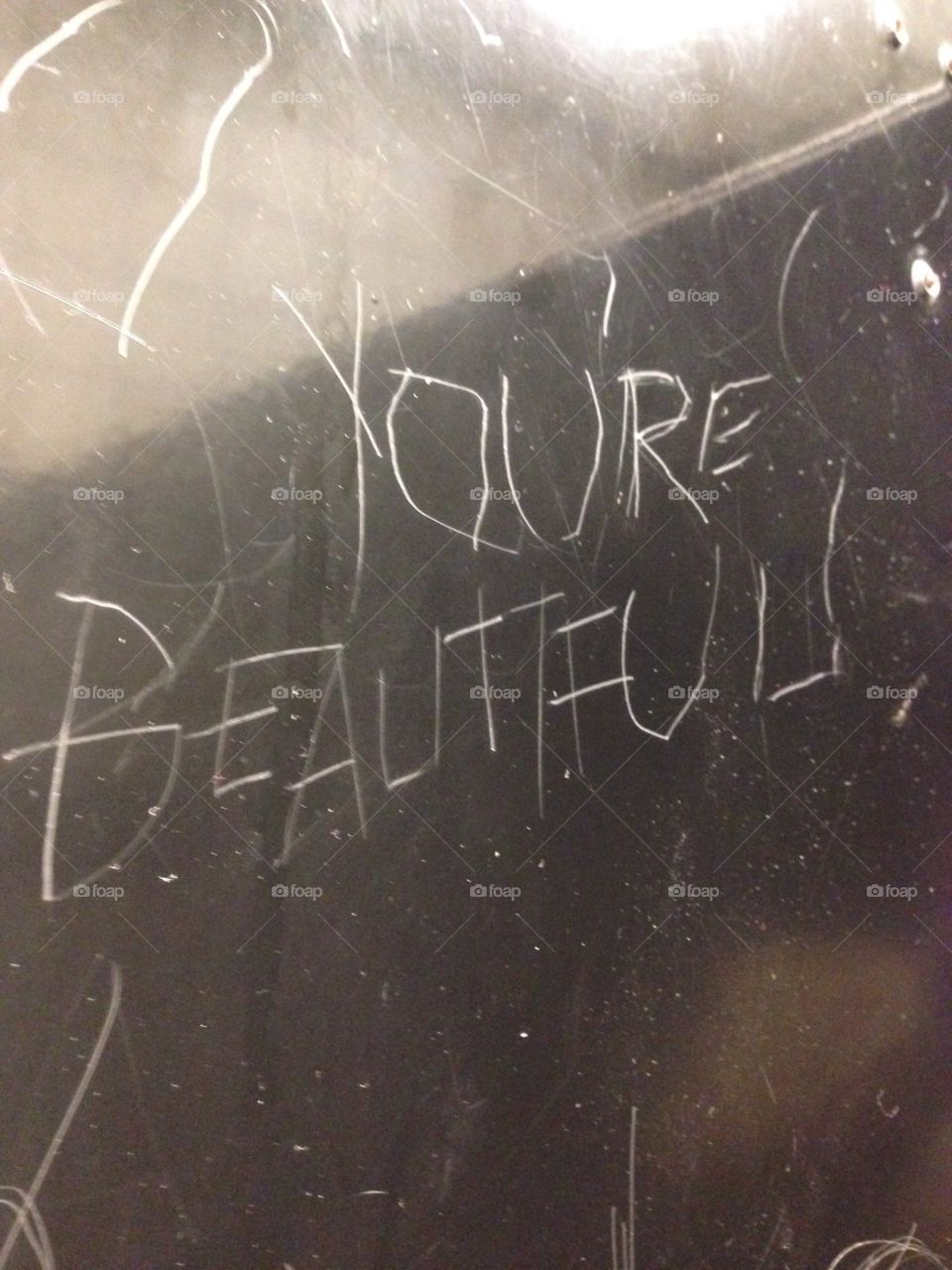 Message scratched on a steel bathroom stall wall, you’re beautiful! Inscription 