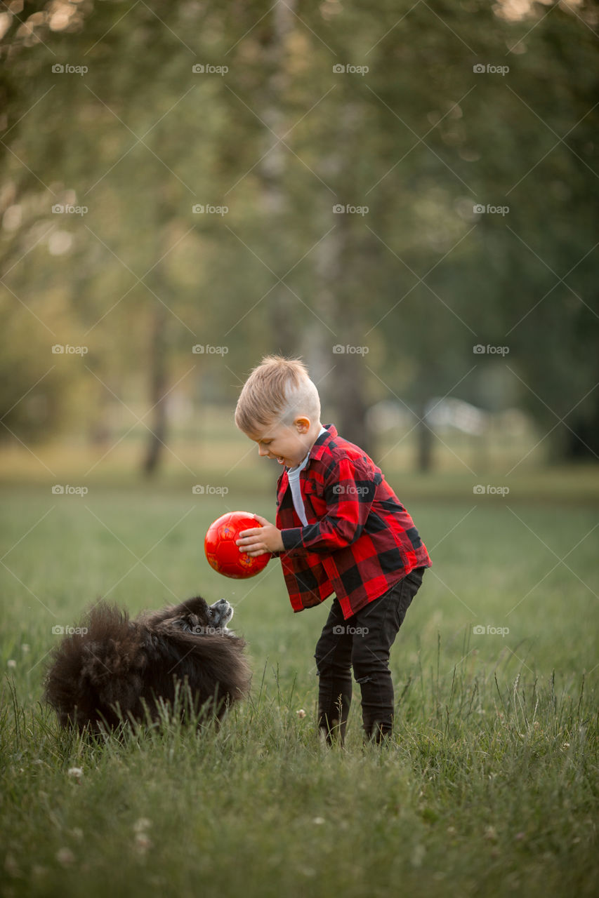 Little boy playing with his dog in soccer in a park 