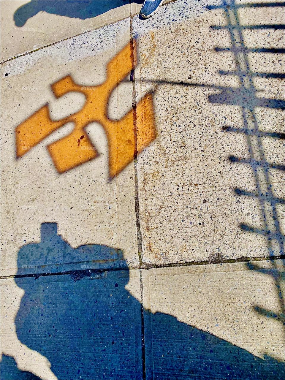 Another beautiful impression created by an urban art installation in LIC, Queens, NY. The intricate shape of the semi opaque orange geometric shape attached to a city fence is cast onto the sidewalk by the sunlight. 2022. Hypnotic Productions