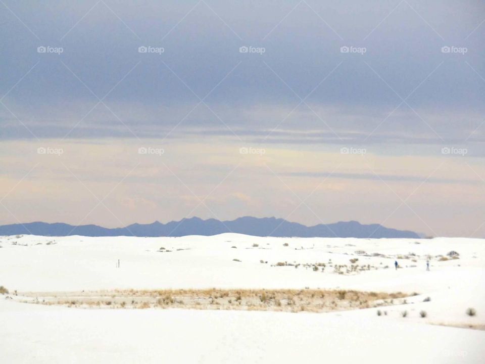 Purple mountains seen in the distance beyond white sand dunes. 