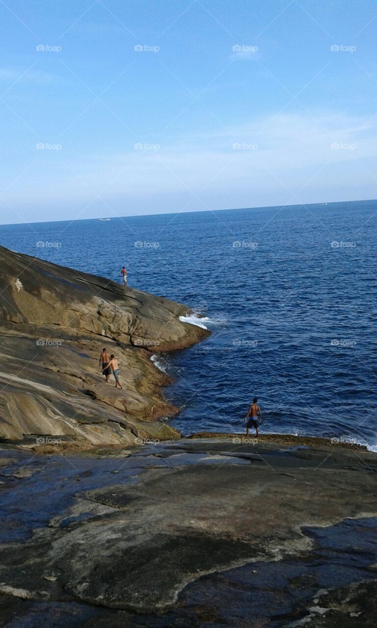 Pessoas na rocha, paisagem à beira mar.