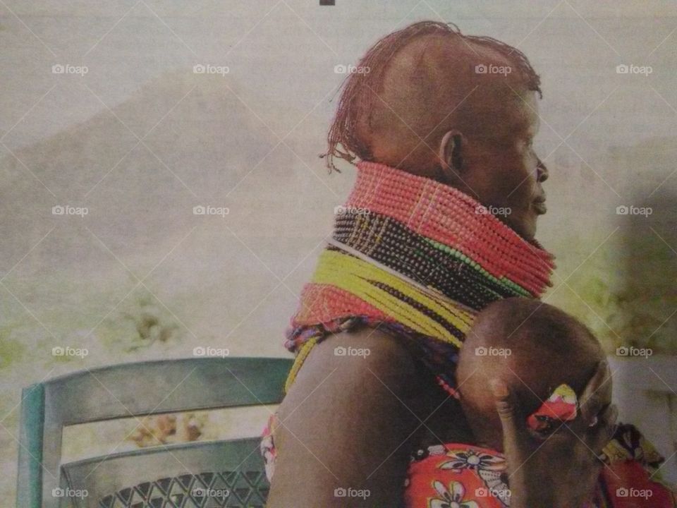 An African woman with her little one during a traditional cultural festival. She's wearing beautiful beaded necklaces.