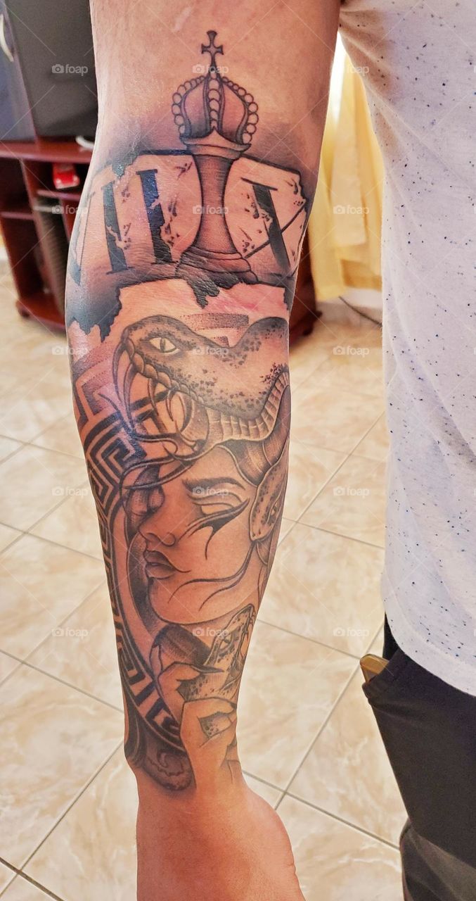 Tattoo of Medusa in the bottom of arm and Roman date of father's year born and year that died, with a Chess King as his father figure on the top of the arm.