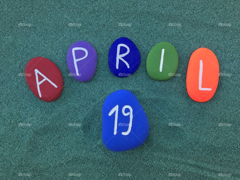 19 April, calendar date with colored stones on green sand 
