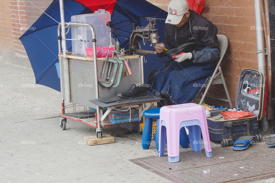 A shoemaker at work on the street repairing shoes in Brooklyn, New York City.