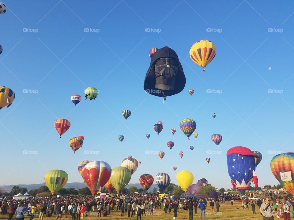 Colorful bright hot air balloons floating above a crowd of people with a black Darth Vader balloon prominent