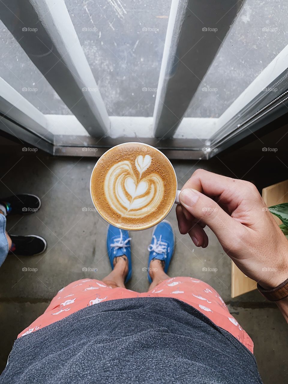 Holding a cappuccino next to a window.