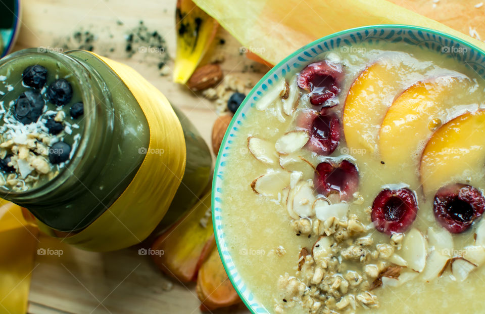 Fresh fruit gourmet smoothie bowls garnished with peaches, cherry,  almonds, blueberry, oatmeal, chia seed, in white and green smoothie flavors on table with healthy ingredients artisanal food and drink -  symbolizing health and happiness photography 