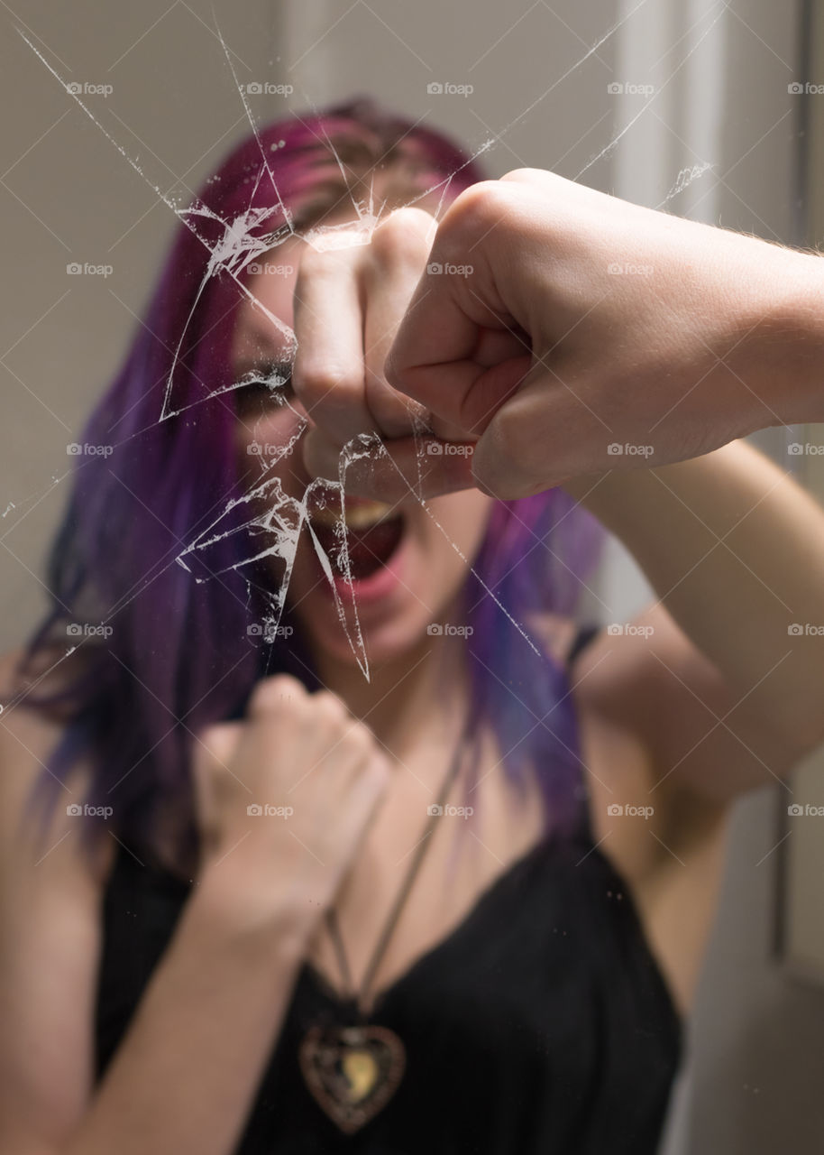 angry girl with low self esteem screams and punches the reflection of her own face in a mirror