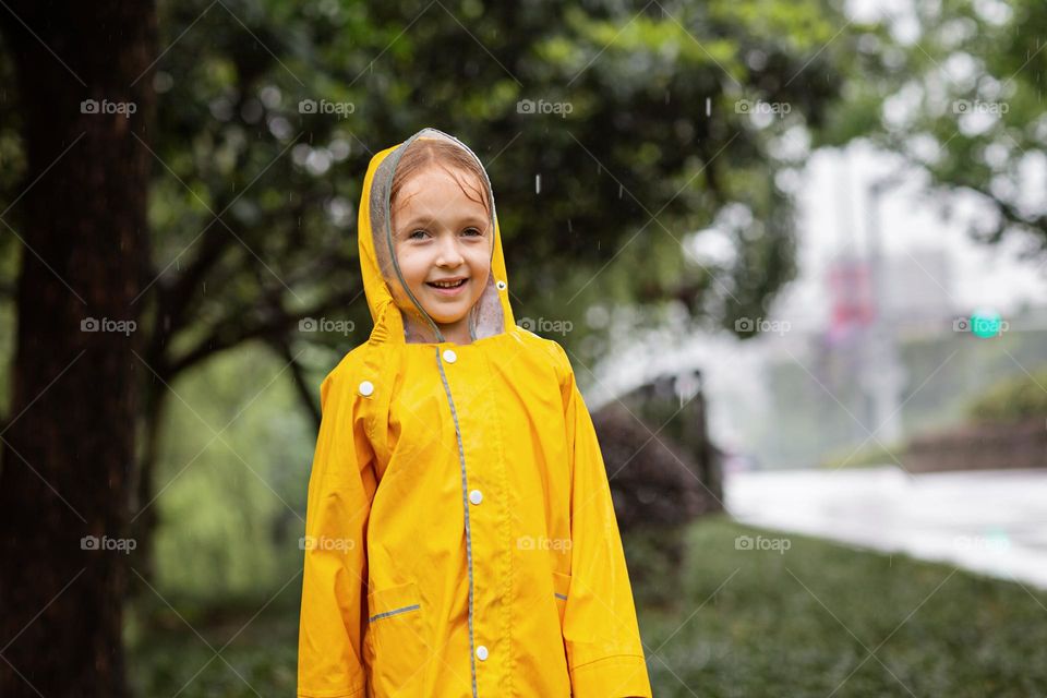 Cute little Caucasian girl with smiley face wearing yellow raincoat outdoor 