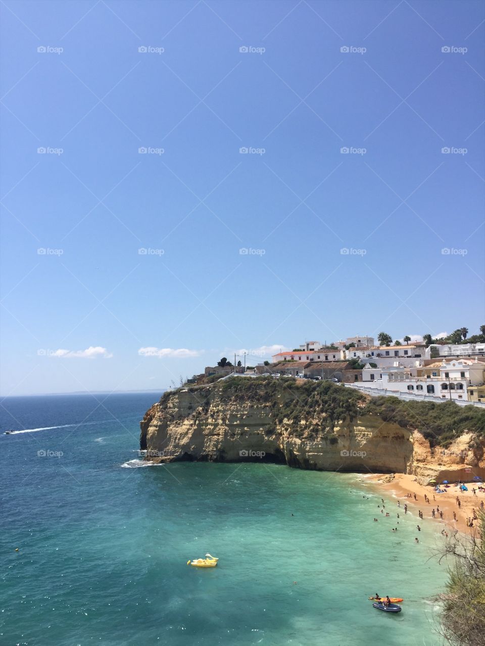 A stunning image of the rocky beaches of the Algarve coastline in southern Portugal, featuring a deep blue ocean and sunny blue skies.