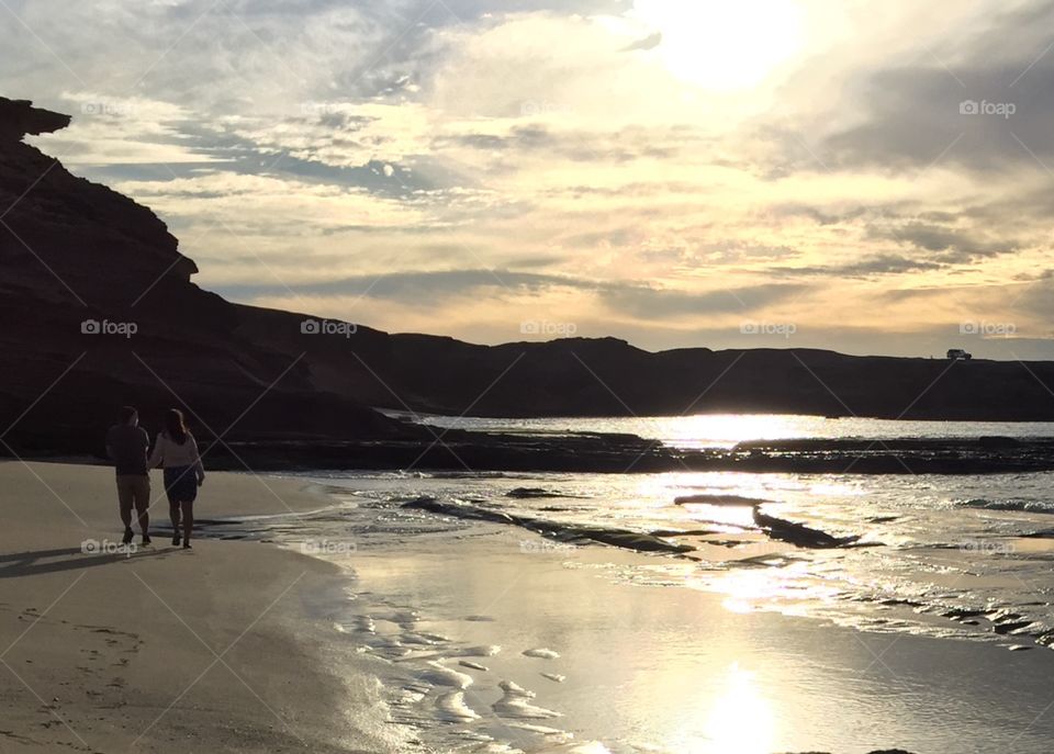 Couple on a beach at dusk with clouds and reflections on water