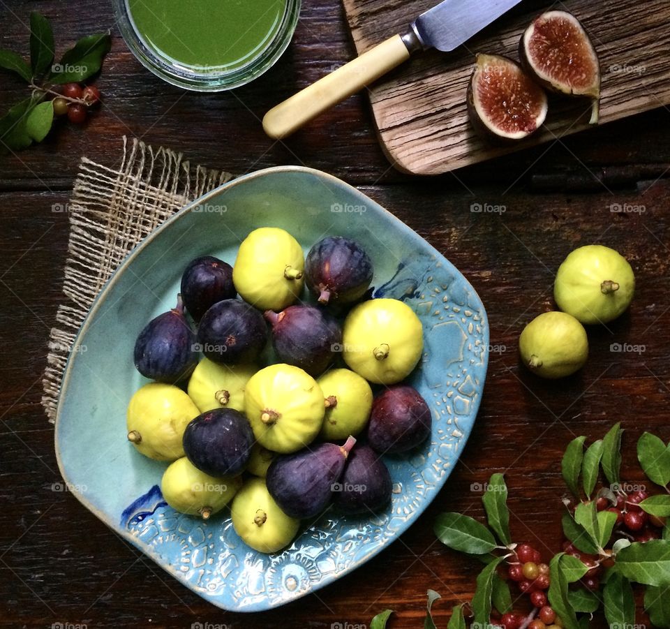 Fresh fruit platter with figs and cutting board with knife and green juice on rustic wood table. 