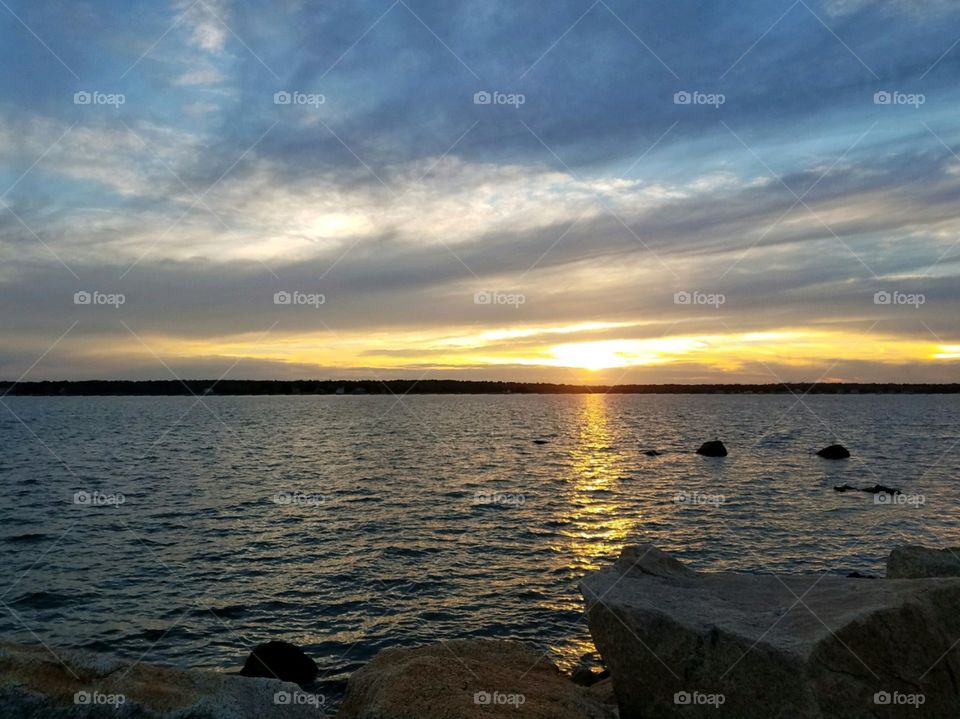 Sunrise, sunset looking from rocky shore of New England. Low sun reflects into water & lights up cloud formation. The colors of sky is beautiful!