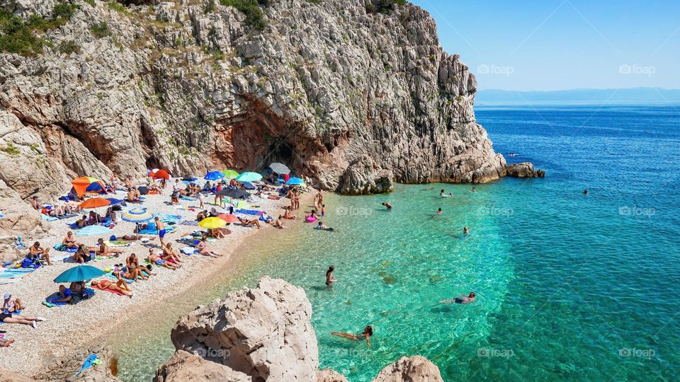 Crowds of people sunbathing on amazing beach in cove with turquoise water at Brsec in Croatia