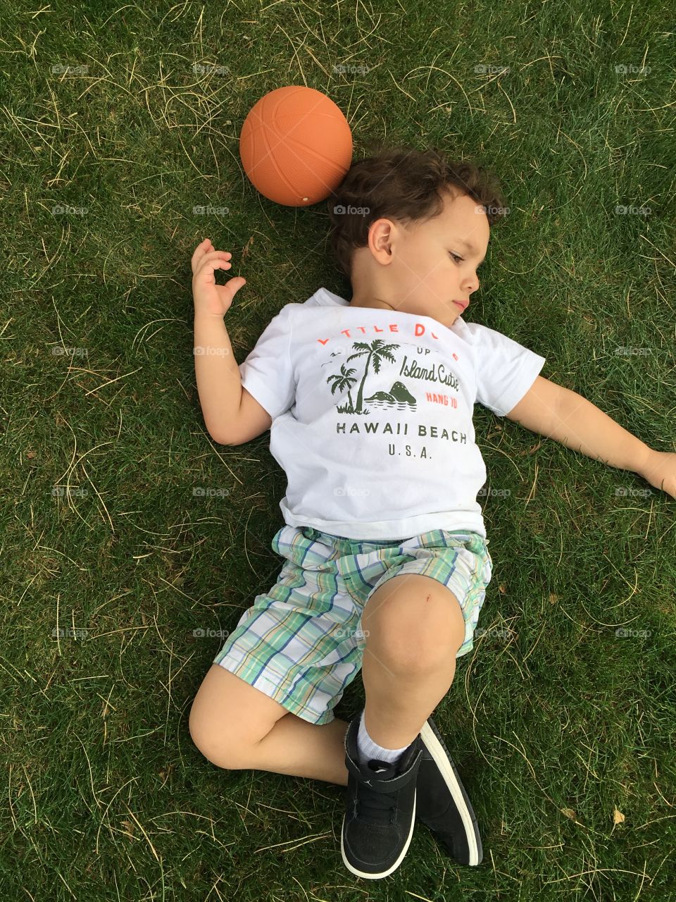 Little boy laying on the grass with his ball.